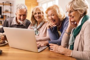 Group of happy mature friends having fun while surfing the net on a computer at home.